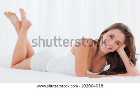 A woman lying in bed with her head in her hand, smiling as she looks forward, with her legs raised up.