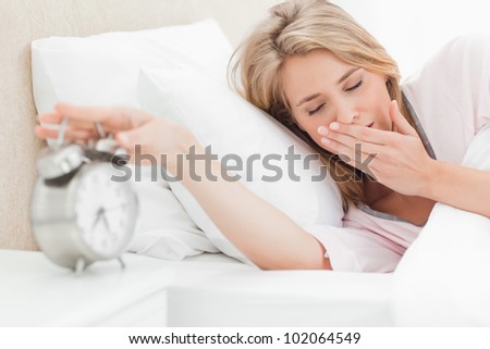 A woman in bed is moving her hand to turn off her alarm, while her eyes are closed