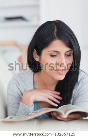 Woman reading a book while lying on a couch and touches her hair in a living room