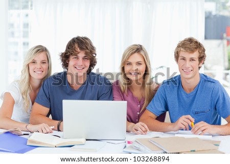 A smiling group of students with a laptop look ahead into the camera