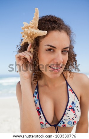 Young woman holding a starfish next to her head while standing on the beach
