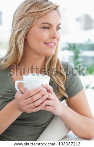 A close up shot of a woman with her head turned to the side while holding a mug in her hands and smiling.