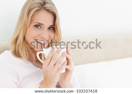 A woman with her head turned slightly and smiling, with a cup in her hands raised to her lips.