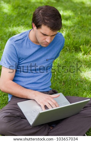 Young serious man using his laptop while sitting in the countryside