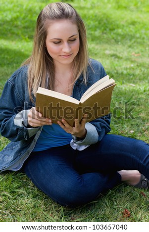Young peaceful girl reading a book while sitting on the grass in a public garden