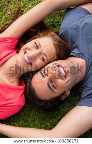 Two friends smiling while lying head to shoulder with an arm out-stretched on the grass