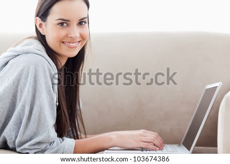A head and shoulders shot of a smiling woman as she looks into the camera with her laptop on the couch