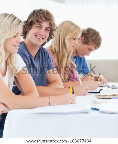 A close up shot of a smiling student sitting with his friends as he looks into the camera