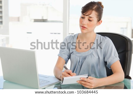 A business woman with a notepad takes notes down from her laptop