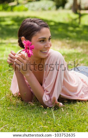 Smiling woman lying down in grass while looking towards the side and holding a flower in her hand