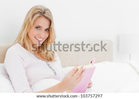 A Side angle shot of a woman sitting forward in bed, her book in hand, with her head turned to the side.