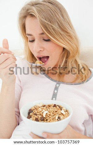 A close up shot of a woman holding a bowl of cereal and a raised spoon of cereal she is about to eat.