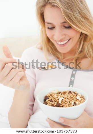 A close up shot of a woman holding a bowl of cereal and a raised spoon of cereal near to her mouth.