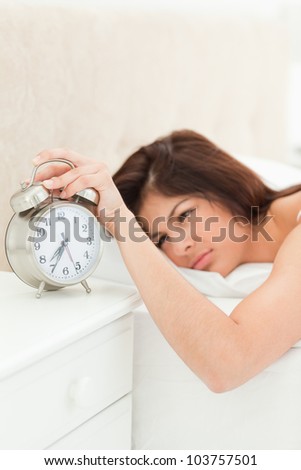 The alarm clock which is showing the time is being silenced by the woman\'s hand who is beside it lying on her bed while fully awake.