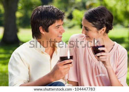 Man and a woman looking at each other while each holding glasses of red wine in a park