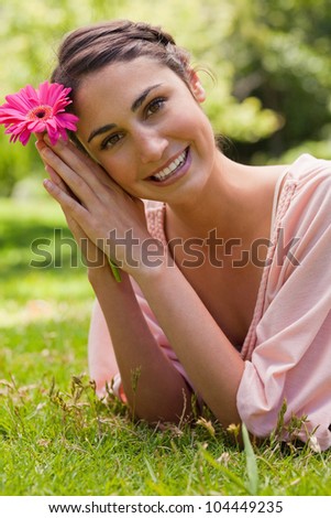 Woman lying on her front with her head turned towards her side as she rests her head against her arms while holding a pink flower
