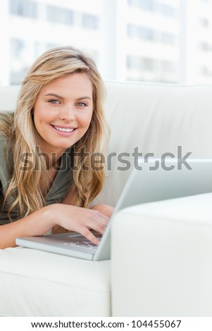 A close up shot of a woman on the couch, using her laptop with smiling and looking in front of her.