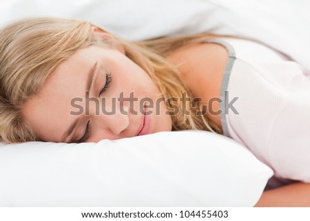 A woman lying in bed, as she rests her head on a pillow here eyes are closed.