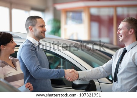 Smiling salesman shaking a customer hand in a car shop