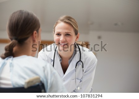 Smiling doctor looking at a patient on a wheelchair in hospital hallway