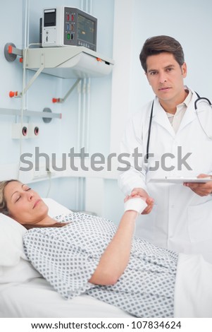 Doctor holding medical result and the hand of his patient in hospital ward