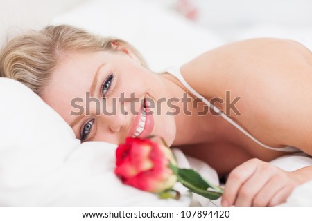 Blue eyed woman smiling with a rose in a bed