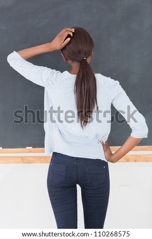 Black woman thinking in front of a blackboard in a classroom