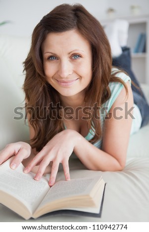 Woman lying on the belly on a sofa touching a book in a living room