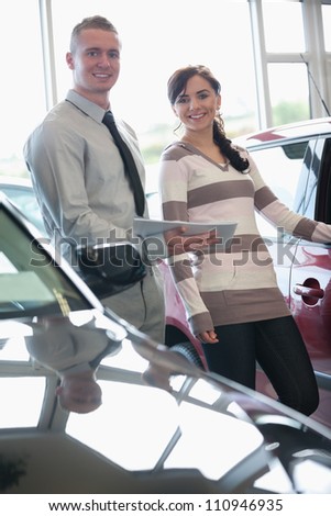 Salesman and a woman standing next to a car in a car shop