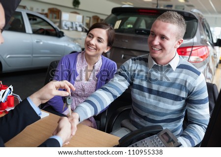 Happy couple shaking the hand of a salesman while receiving car keys