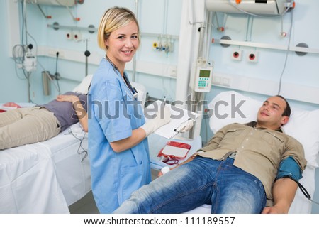 Nurse looking at camera next to transfused patients in hospital ward