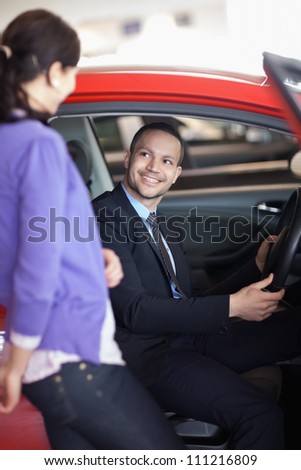 Man sitting in a car while talking to a woman in a car shop
