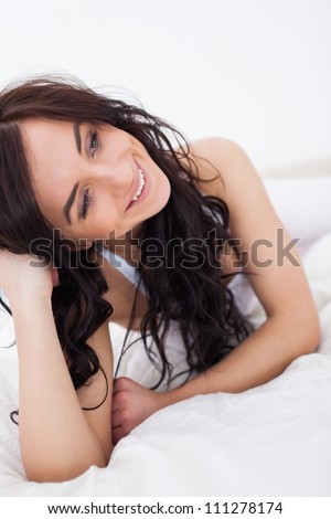 Happy brunette woman lying on her white duvet in her bedroom