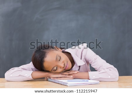 Black woman leaning her head on desk with closed eyes in a classroom