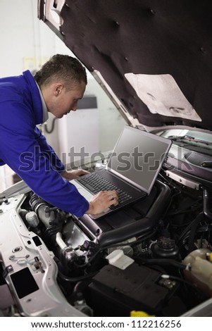 Mechanic looking at a computer on a car engine in a garage