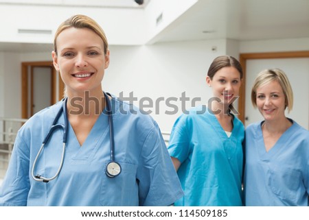 Two nurses in the background and one in the foreground in hospital corridor