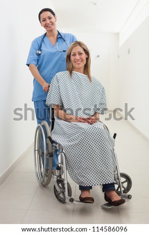 Happy nurse and patient in wheelchair in hospital corridor