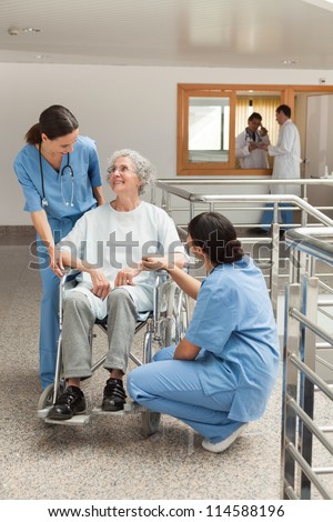 Old woman in wheelchair talking with nurses in hospital corridor