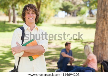 Young man posing with textbook in a park with friends in background