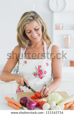 Smiling woman in apron cutting various vegetables