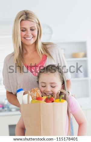 Daughter looking into grocery bag with mother watching in the kitchen