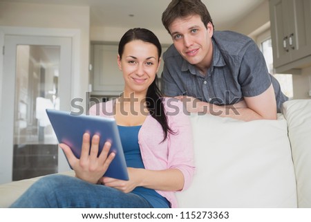 Woman sitting on the couch with a man behind her while using the tablet computer