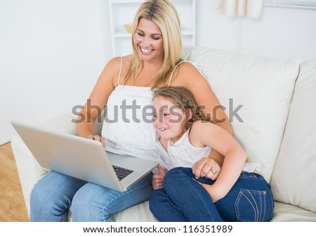 Laughing mother and daughter using notebook during resting on sofa