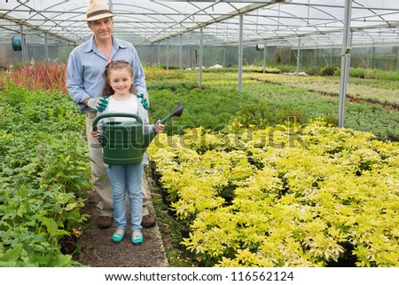 Gardener with granddaughter holding watering can in greenhouse