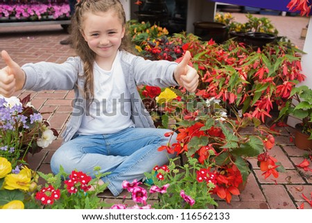 Little girl giving thumbs up while sitting on the floor with flowers around her