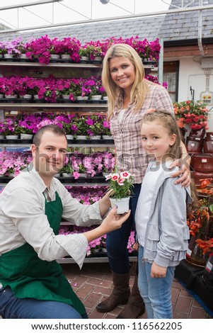 Employee giving flower pot to little girl with mother in garden center
