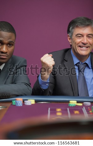 Smiling man sitting at table in a casino and celebrating roulette win