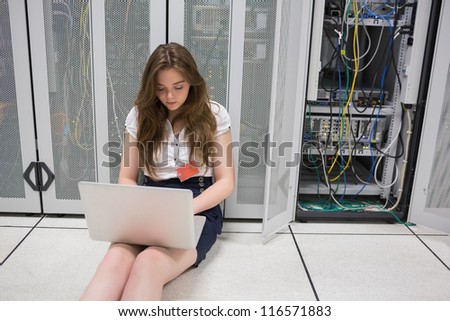 Woman working on servers with laptop sitting on the floor in data center