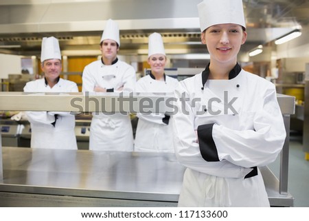 Smiling chef standing with her arms crossed with team standing behind her