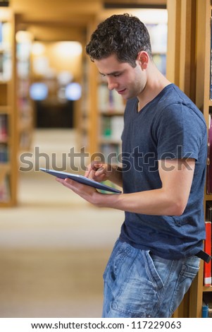 Man leaning against book shelf using tablet pc in college library